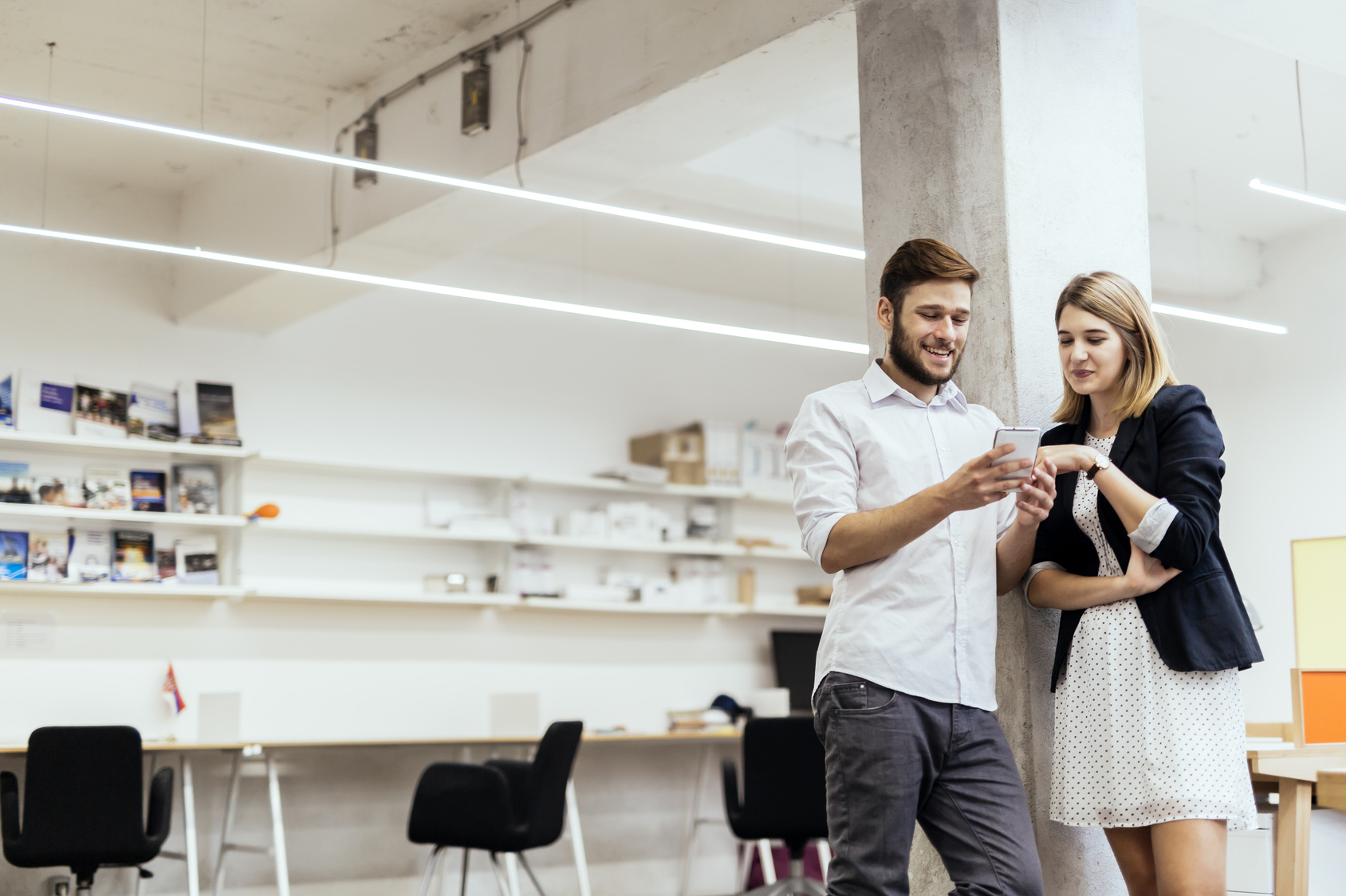 Two colleagues smiling while looking at the phone in a beautiful office